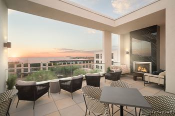 A roof top patio with a fireplace and chairs overlooking a cityscape at sunset.